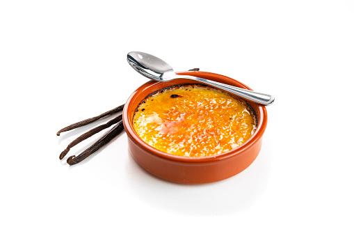 Sweet food: high angle view of a clay bowl with Creme brulee shot on white background. Copy space. Vanilla beans complete the composition