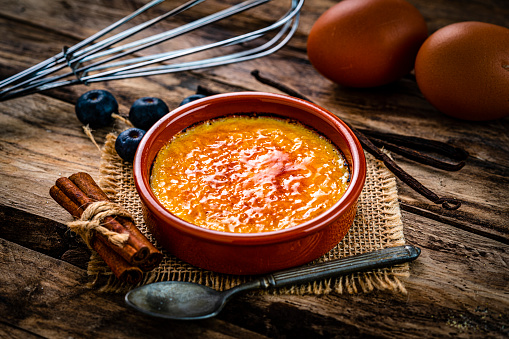 Sweet food: close up view of a clay bowl with Creme brulee shot on rustic wooden table.