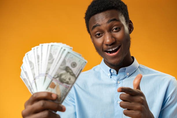 istock Excited black guy holding stack of Dollars in yellow studio 1385723431