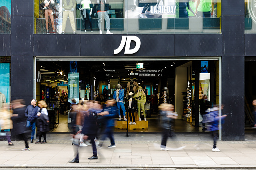 London, UK - 14 March, 2022: color image depicting the exterior of a JD sports clothing store in central London, with blurred motion of people walking past on the street outside the shop.