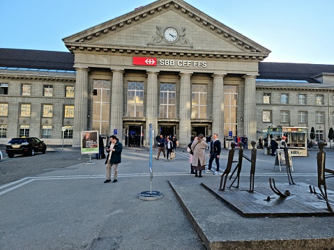 Biel/Bienne railway station serves the bilingual municipality of Biel/Bienne, in the canton of Bern, Switzerland. The building was realized in 1923. The image shows the main entrance with several people before it.