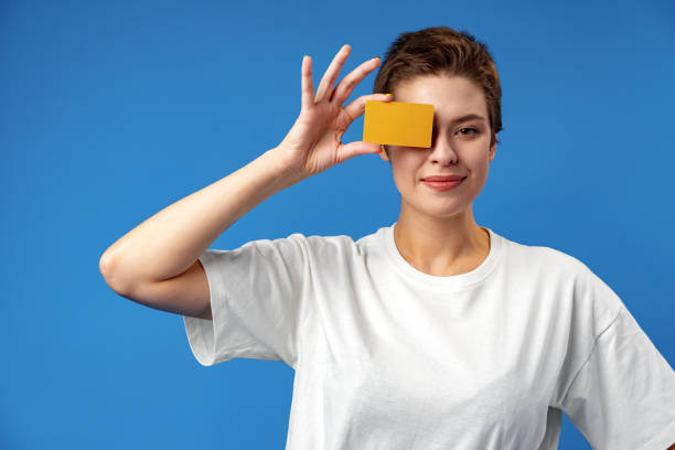 imagen de una mujer joven sosteniendo una tarjeta de visita con espacio de copia sobre fondo azul - invitation blank smiling business card fotografías e imágenes de stock