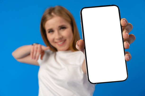 istock Young smiling woman showing blank screen smartphone in studio 1385729289