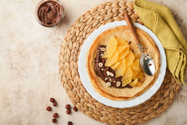 istock Crepes suzette with oranges. Thin crepes with chocolate spread, hazelnuts and orange slices fruit in white plate for breakfast on old concrete rustic table background. Copy space . Top view. 1385729366