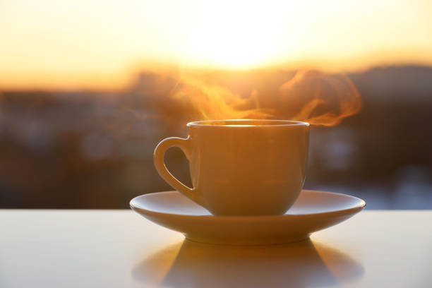 istock Hot coffee or tea cup with smoke on sunrise sky background 1385731685