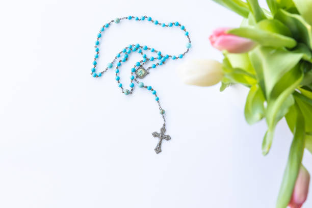 blue rosary prayer beads on a white background with border of fresh pink and white tulips with copy space