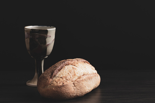 Clay chalice and loaf of artisan bread on a black background with copy space