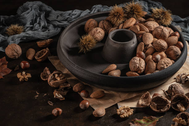 Modern design black ceramic bowl with walnuts, hazelnuts, almonds, chestnut hedgehogs on dark countertop and background. Autumn table
