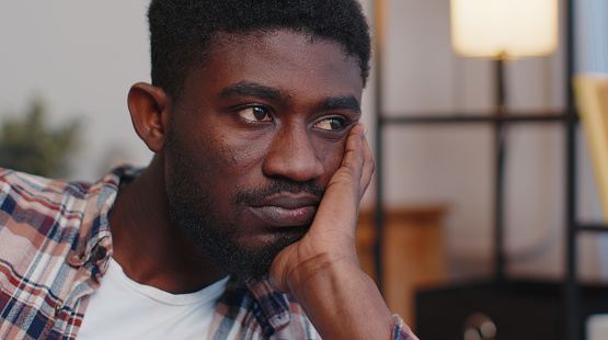 Close-up sad face of african american man sitting at home looks pensive thinks over life concerns or unrequited love, suffers from unfair situation. Problem, break up, depressed feeling bad annoyed