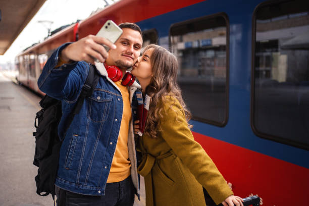 istock Young couple standing at the train station taking selfies while waiting for their train 1385748489