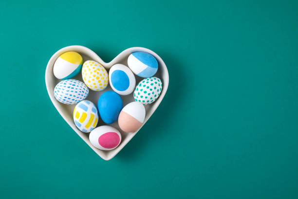 istock Colorful Easter Eggs in Heart Shaped Bowl on Green Background 1385749689