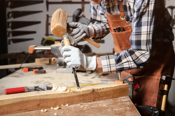 Photo of Skilled carpenter carving wood with hammer and chisel.