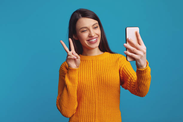 istock Cute woman showing peace gesture while having video-call over blue background 1385757371