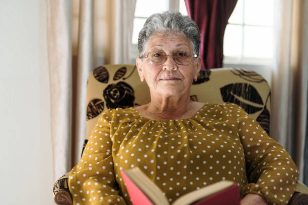 Senior woman sitting holding a book and looking at the camera.