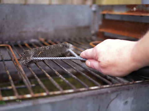 Cleaning dirty bbq grill with brush wide shot selective focus