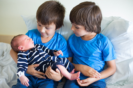 Two boys, brothers, meeting for the first time their new baby brother at hospital. Family happiness concept