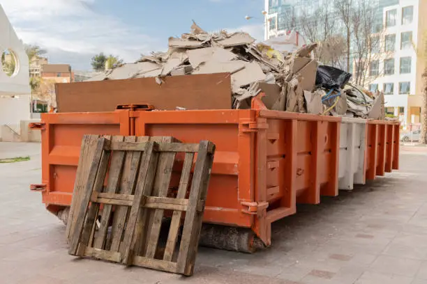 Photo of huge heap on metal Big  Overloaded dumpster waste container filled with construction waste, drywall and other rubble near a construction site.