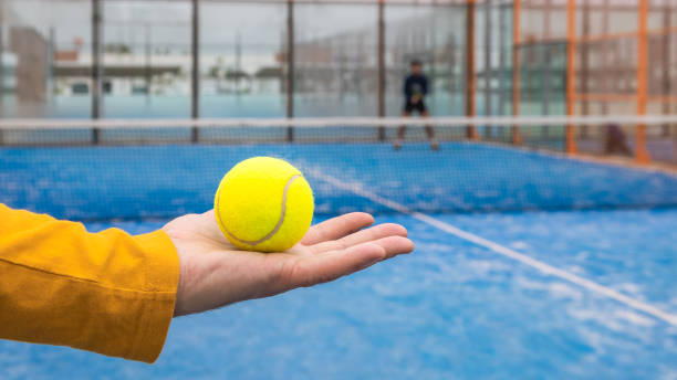 Male hand holding paddle tennis ball. Professional player starting set in court Male hand holding paddle tennis ball. Professional player starting set. Men playing a match in the open. Man playing padel on a blue grass court outdoors behind the net paddle ball stock pictures, royalty-free photos & images