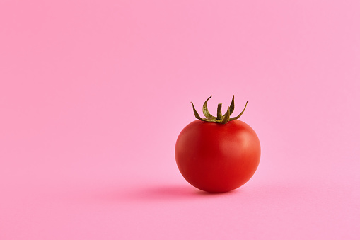 Single organic ripe and fresh red cherry tomato isolated on pink background in the studio