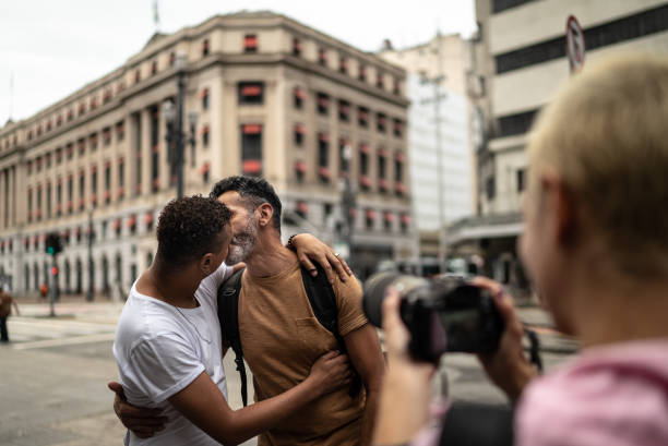 Young woman photographing a gay couple kissing in the street Young woman photographing a gay couple kissing in the street tourist couple candid travel stock pictures, royalty-free photos & images
