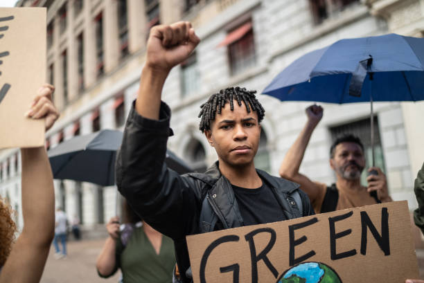 junger mann mit einem schild während einer demonstration auf der straße - klimaschutz stock-fotos und bilder