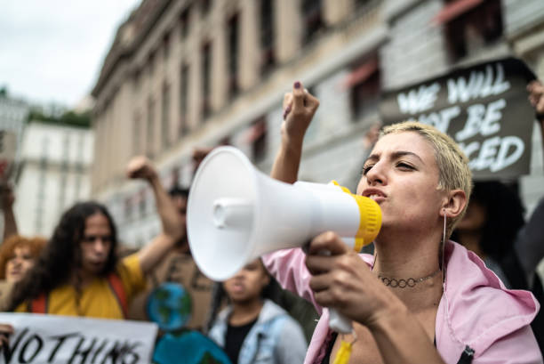 joven liderando una manifestación usando un megáfono - protest fotografías e imágenes de stock