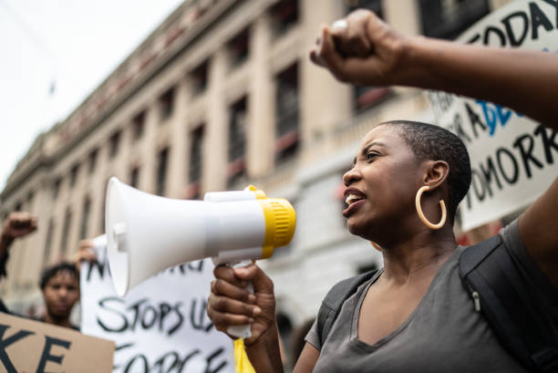 mid adult woman leading a demonstration using a megaphone - protesto imagens e fotografias de stock