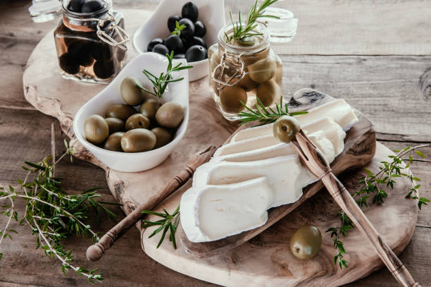 oliven sind grün und schwarz mit weichkäse mit schimmel wie brie, camembert mit olivenöl und thymian. käse und oliven in einem olivenbaumgericht - dishware butter cutting board agriculture stock-fotos und bilder