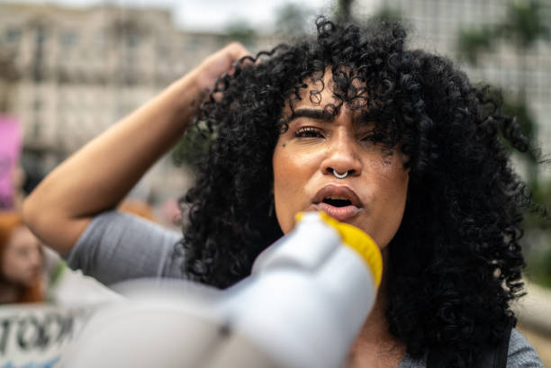 mujer liderando una manifestación usando un megáfono - riot fotografías e imágenes de stock