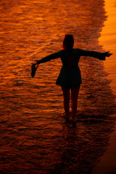 Barefoot woman walking on the beach. The sun is setting.