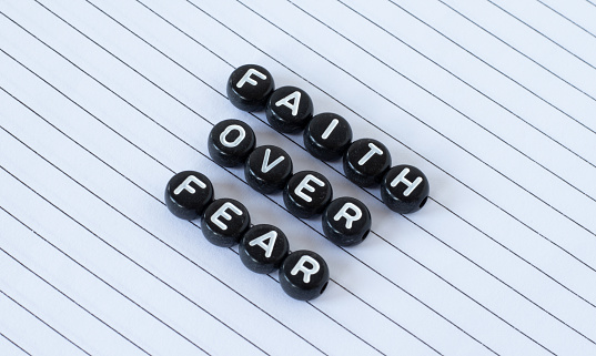 Faith over fear, a quote from the Holy Bible Book written with black circle letters isolated on a white lined paper background. The biblical concept of faith and trust in God Jesus Christ. A closeup.