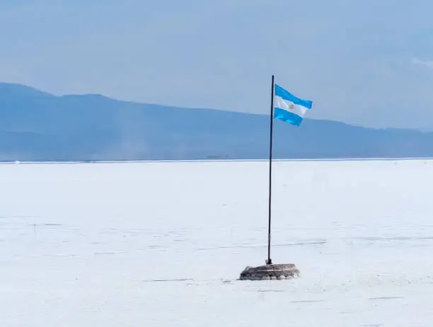 Photo of Argentinian flag in the huge expanses of the Salinas Grandes, an enormous salt flat in the provinces of Jujuy and Salta, Argentina.