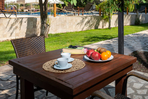 Coffee cups and fruit plate on wooden table by the pool.