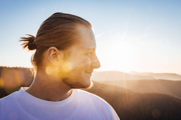 Smiling young millennial generation blonde man in white shirt looking outdoors over towards the sunset. Swabian - South German Mountain Range in the background. Real People Millennial Generation Outdoors Lifestyle Portrait.