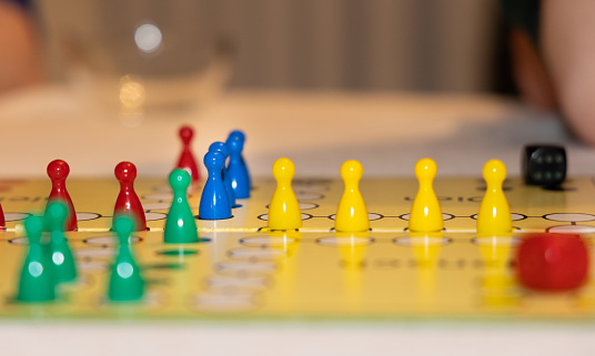 close up view of a board game with colorful game pieces -  focus on one game piece with reduced field of depth. Blurred foreground and blurred background. red and black dice.