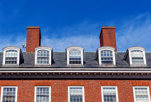 Dormer windows along roof line of residential building against a blue sky.