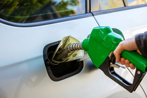 Conceptual photo showing inflation and economic impact at the gas pump with hundred dollar bills inside the tank