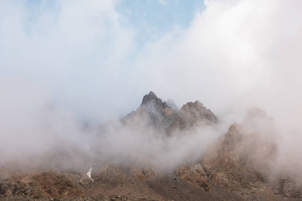 아침 햇살에 울창한 낮은 구름에 바위 산과 경치 알프스 풍경. 두꺼운 낮은 구름 사이 날카로운 바위와 다채로운 산 풍경. 낮은 흐림에 높은 로키에 멋진 보기. - dense fog 뉴스 사진 이미지