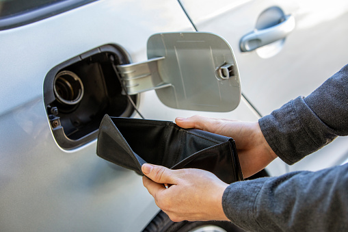 A man holding open an empty wallet at the gas at the station showing inflation and economic impact at the gas pump.