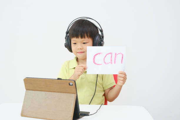 istock Little Asian child using tablet pc studying online lesson at home, Kid learn to read via e-learning 1385865224