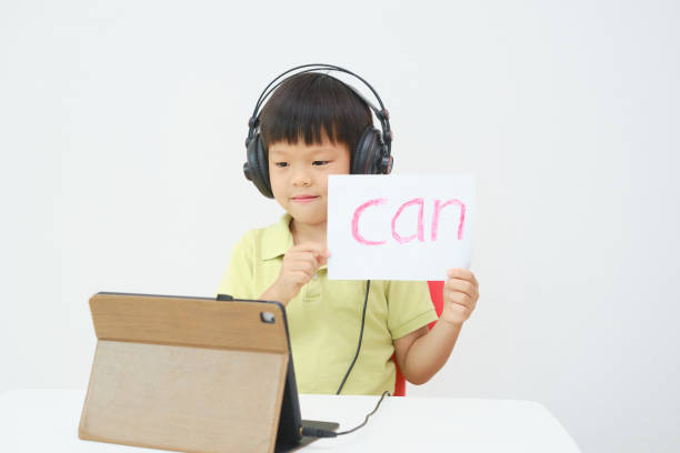 Little Asian child using tablet pc studying online lesson at home, Kid learn to read via e-learning stock photo