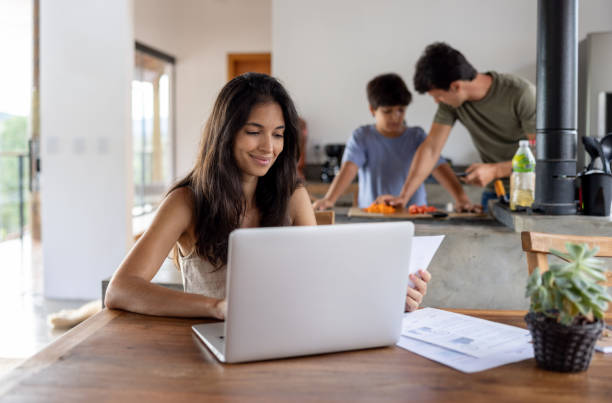 istock Mother working at home while her husband and son cook at the background 1385871601