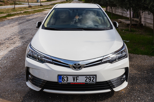 Side; Turkey – February 28 2022:  white Toyota Corolla   is parked  on the street on a warm  day against the backdrop of a buildung, trees