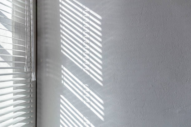 istock sunlight through a window of blinds. shadows on the white stucco wall. 1385879286
