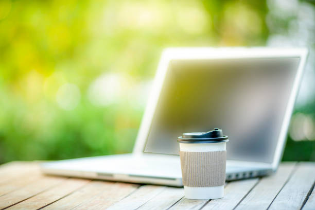 istock coffee cup paper with a Computer laptop in green nature background. Work remotely or from home. soft focus.shallow focus effect. 1385882370
