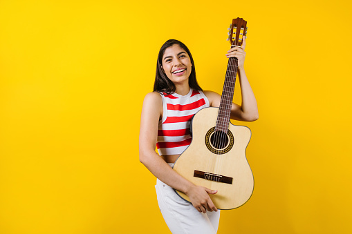portrait of young latin woman holding a guitar on music concept and copy space on yellow background in Latin America