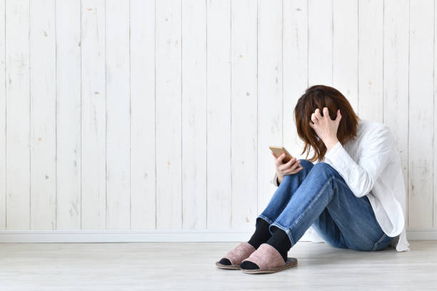 リビングルームで髪を傷つけたスマートフォンを使用している女性 - 悔しい ストックフォトと画像