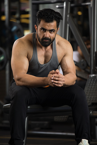 Portrait of muscular man sitting with hands clasped while taking a break at gym