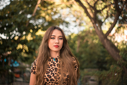 A beautiful young asian woman with long dyed hair wearing a leopard print dress, at the park.