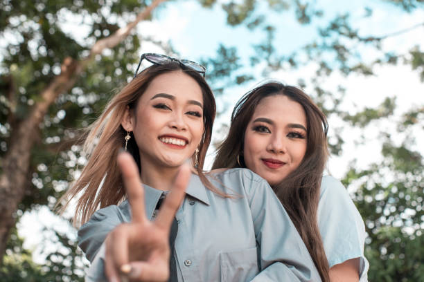 Two young best friends pose for the camera while at the park. One gestures a peace sign. Fun bonding times. Two young best friends pose for the camera while at the park. One gestures a peace sign. Fun bonding times. filipino family stock pictures, royalty-free photos & images